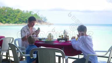 一家有孩子的家庭在海滩上的一家餐馆吃饭。 户外食品